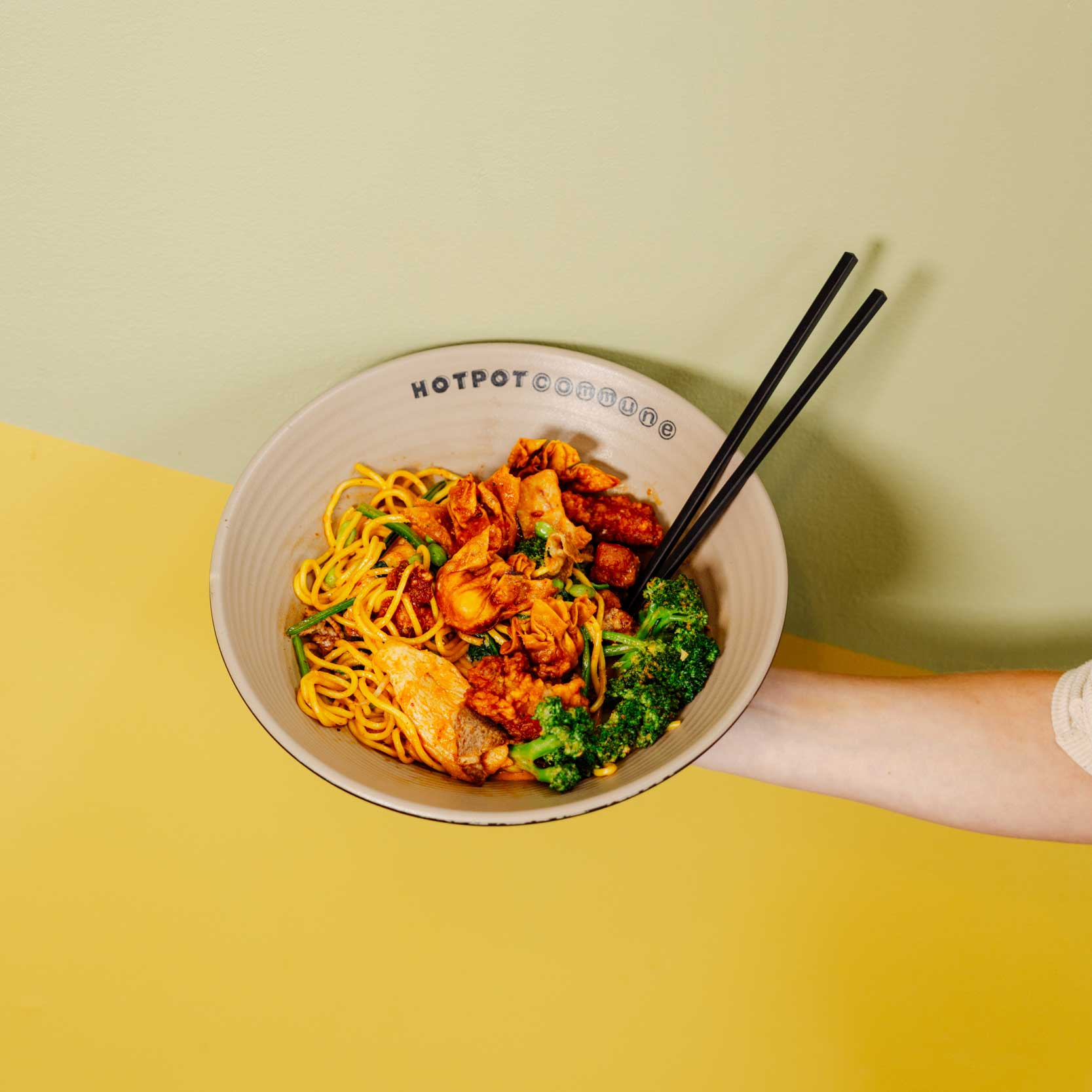 Close-up of chopsticks lifting noodles from a steaming hotpot bowl.